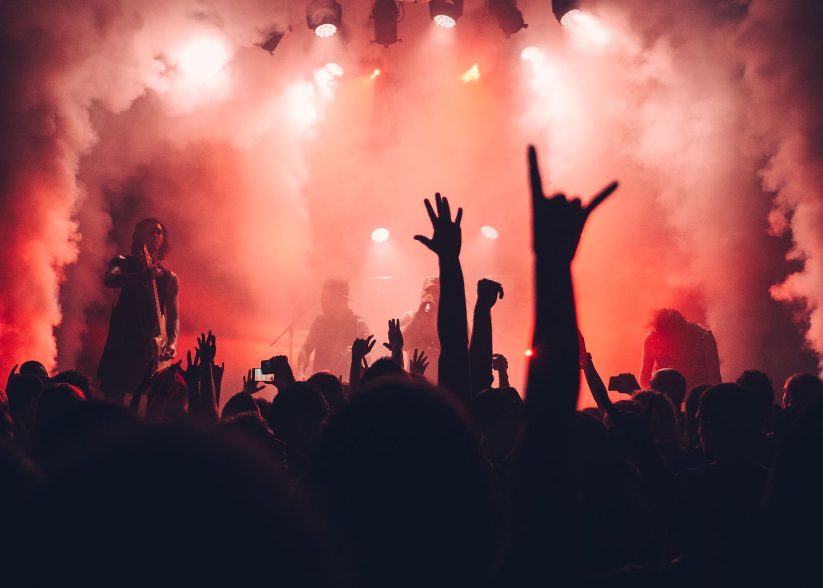 Concertgoers with raised hands illuminated by stage lights.